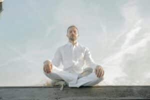A man in a white shirt and tie sitting in a lotus position